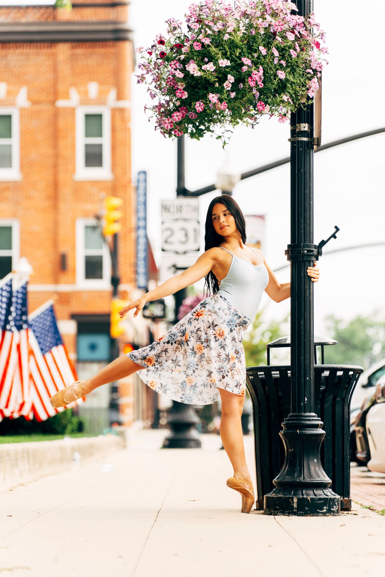 professional Senior portrait photographer captures dancer in floral skirt beside a lamppost on Crown Point Indiana's Main Street.
