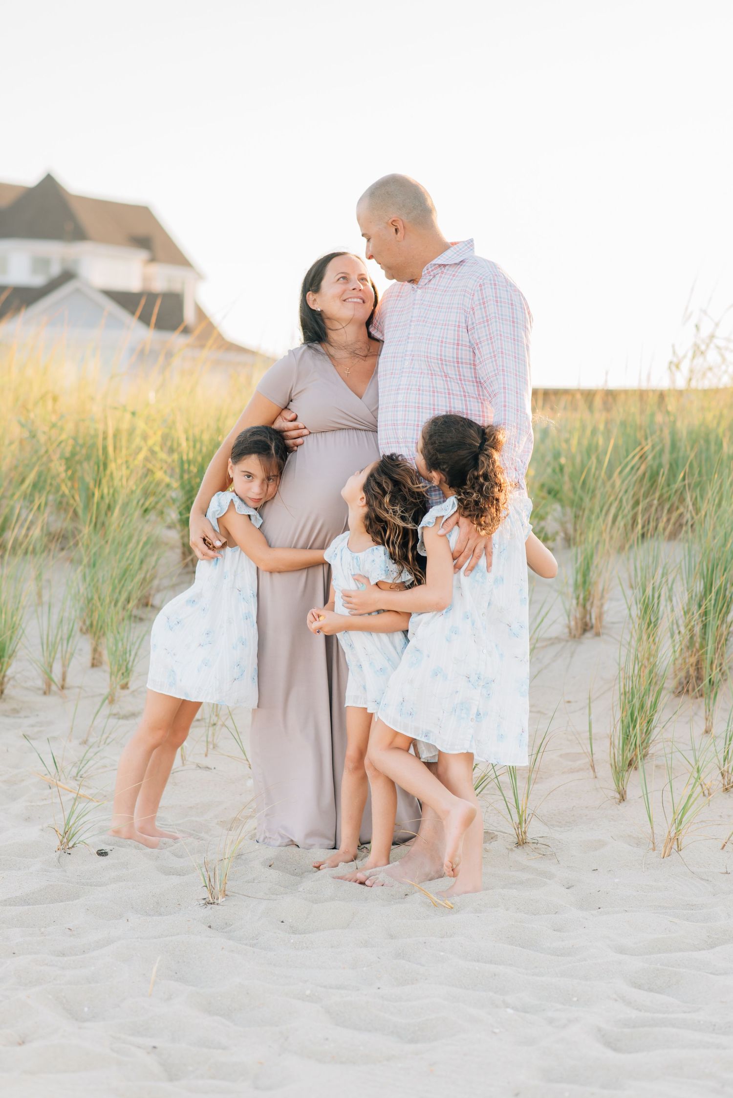 Wide landscape photo of a family of four walking along the quiet shoreline in Monmouth Beach, NJ under a soft pink sunset sky.