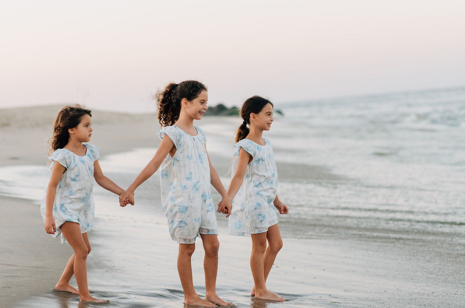 Sisters walking barefoot along the tide in Monmouth Beach NJ, showcasing relaxed beach wardrobe and soft sunset light.