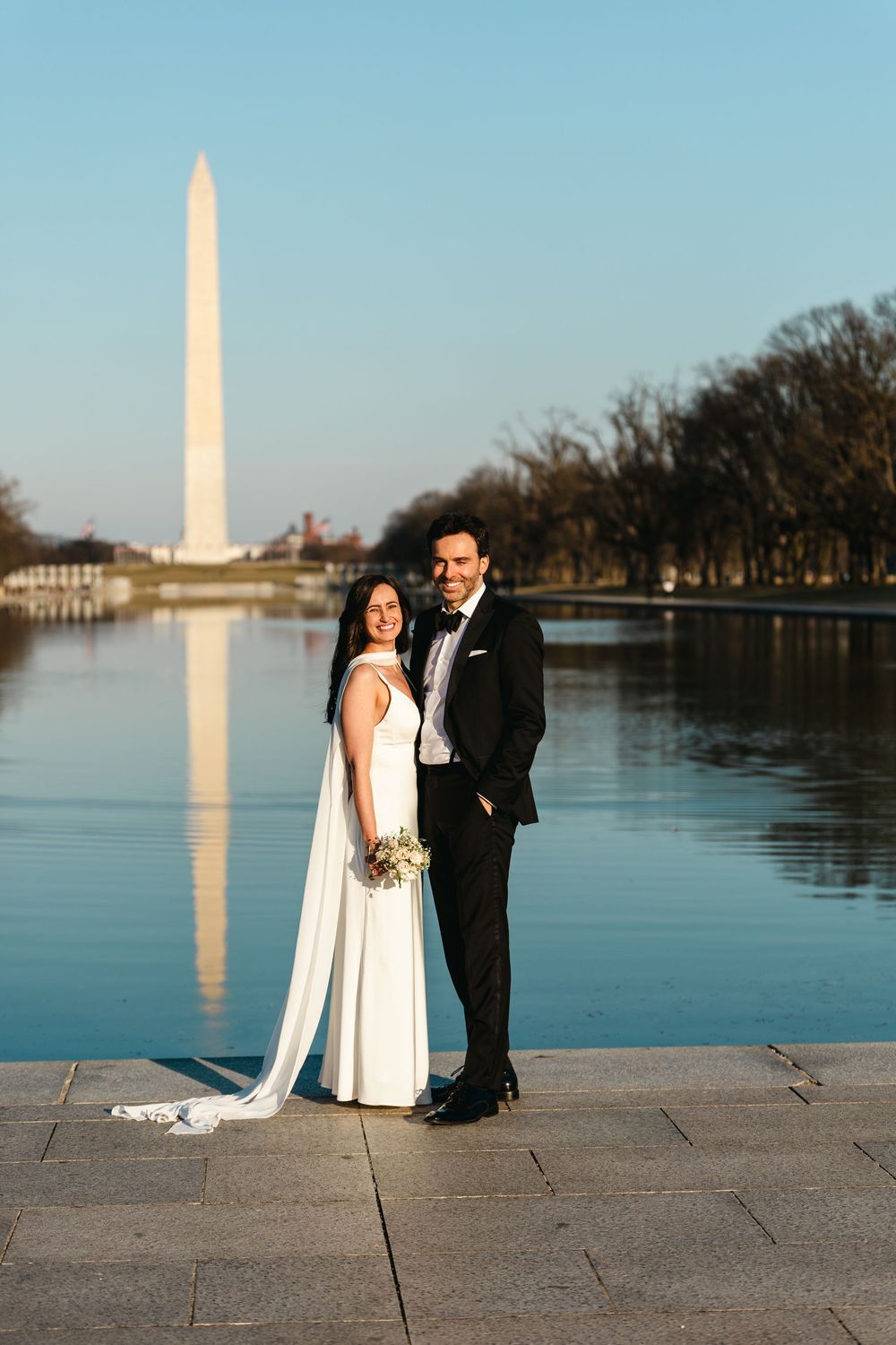 Bride and groom posing by the Reflecting Pool with the Washington Monument in the background on their wedding day.