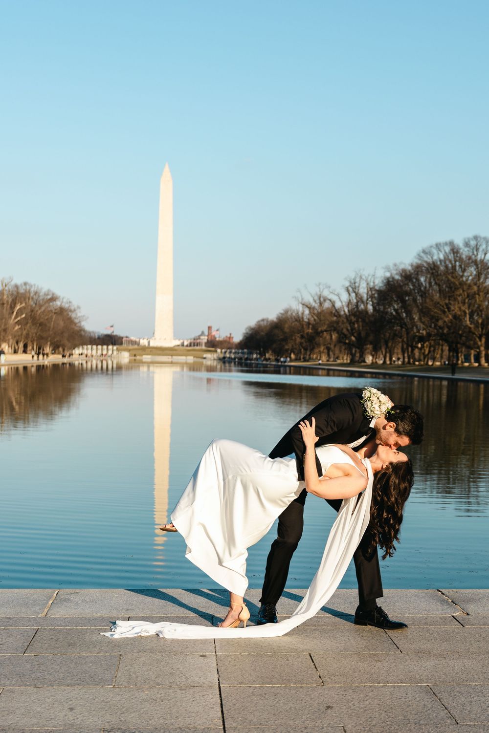 Newlyweds share a romantic dip kiss at the Lincoln Memorial Reflecting Pool with the Washington Monument backdrop.