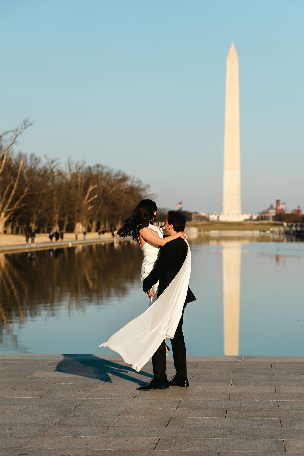 Couple embracing near the Washington Monument reflecting pool during golden hour engagement photos.