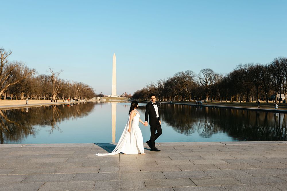 Bride and groom hold hands by the Reflecting Pool with the Washington Monument at sunset in Washington, D.C.