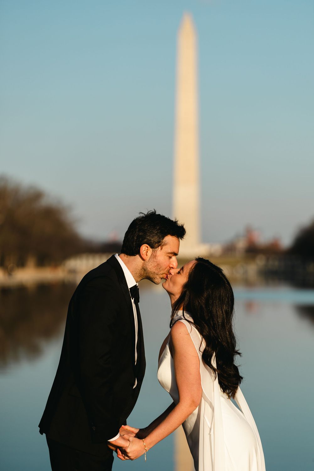 Bride and groom kissing by the Reflecting Pool with the Washington Monument in the background.