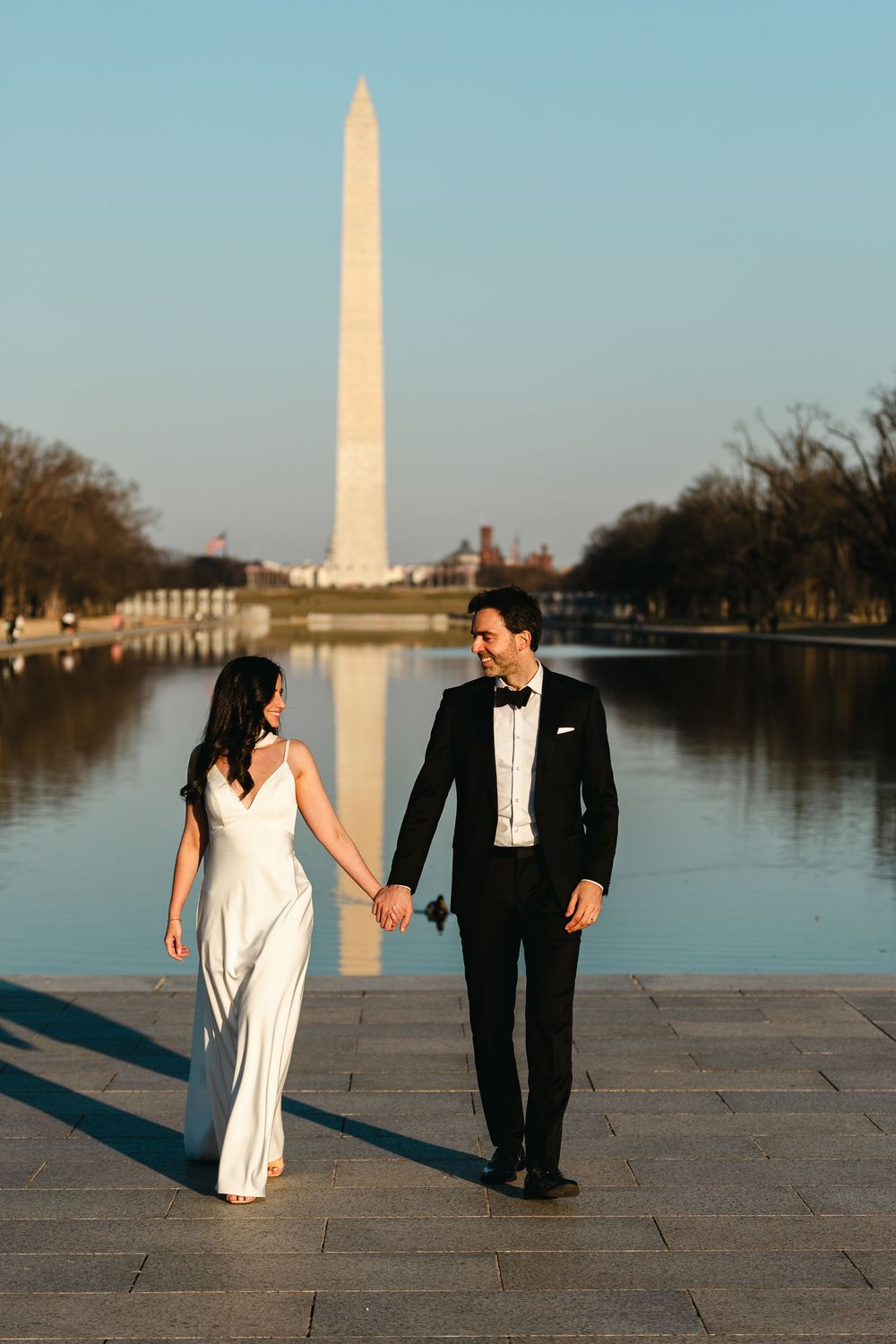 Couple holding hands walking by the Washington Monument reflecting pool in formal attire.