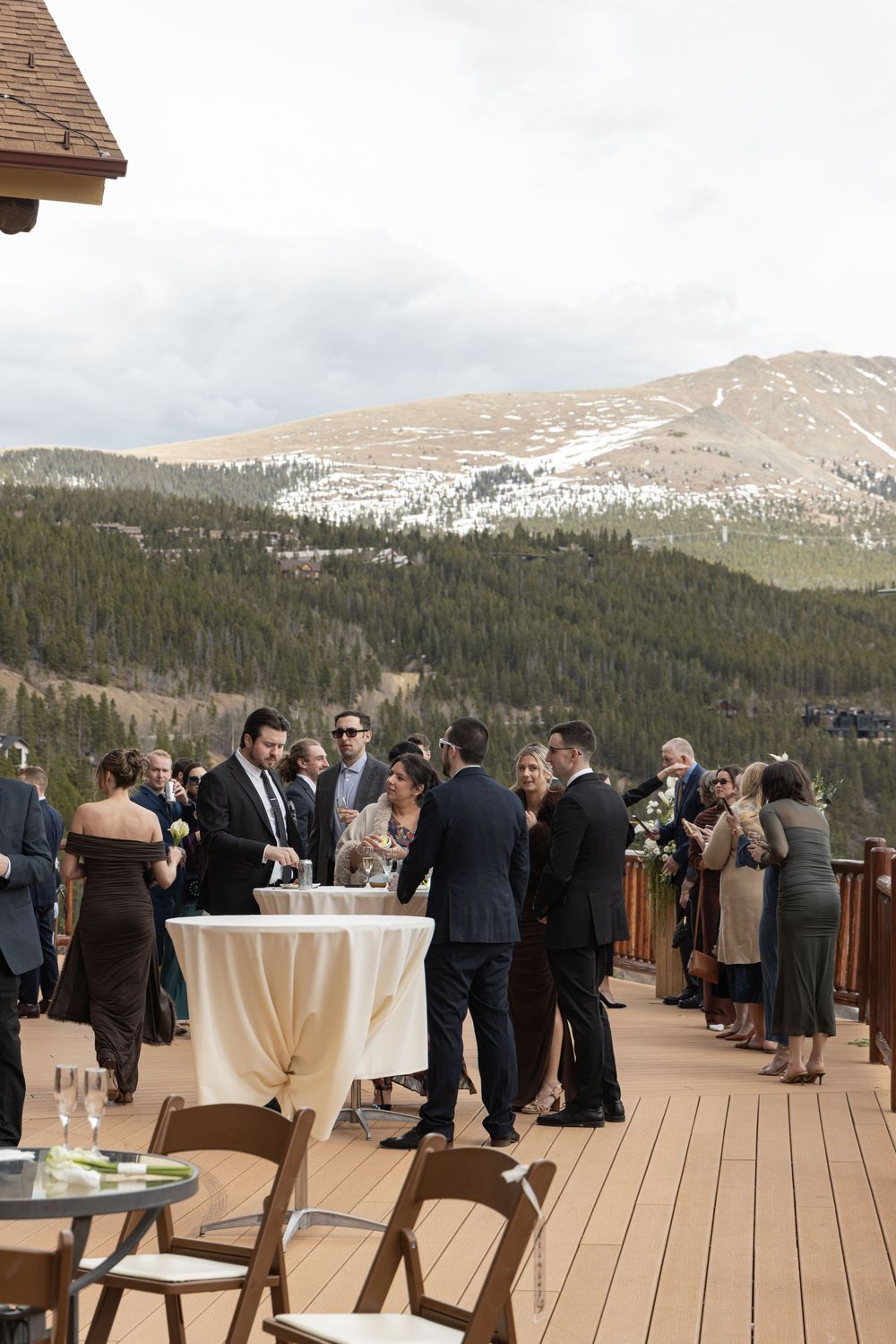 Elegant outdoor wedding reception on a mountain deck with snow-capped peaks and pine forest backdrop.