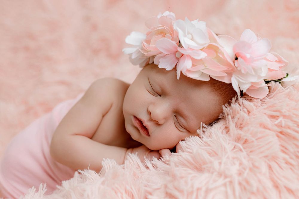 Sleeping newborn baby wearing a pink floral headband, wrapped in pink on a soft fluffy pink blanket.