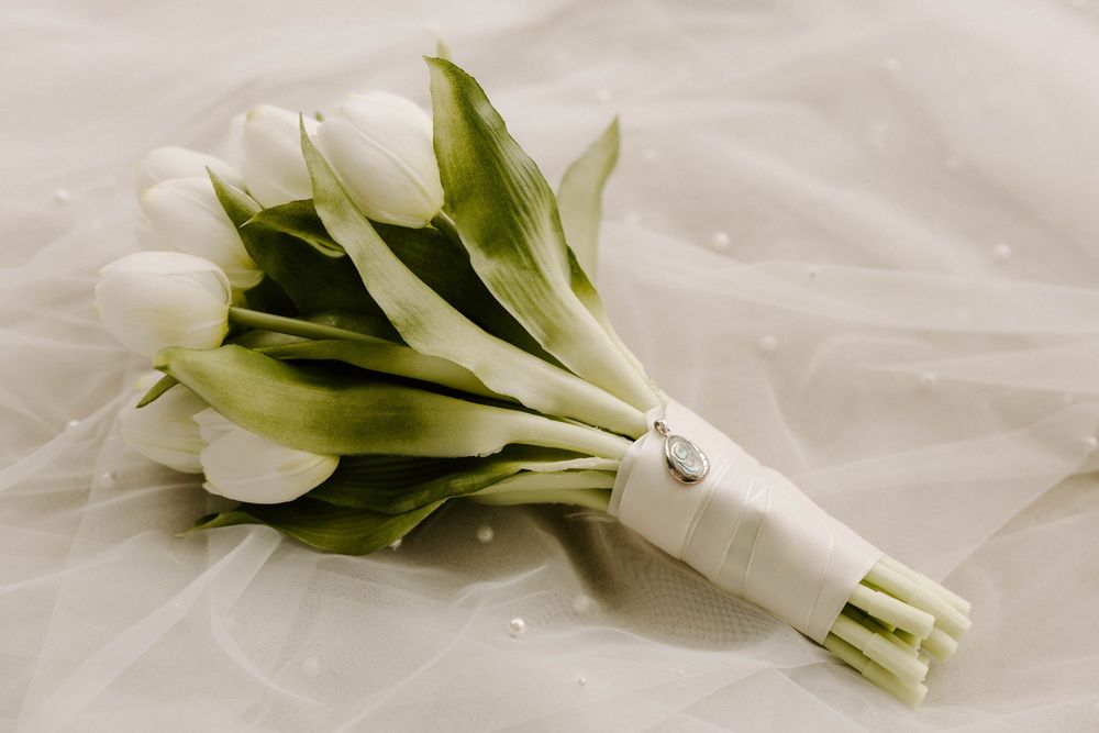 White tulip bridal bouquet wrapped in satin ribbon resting on delicate white wedding veil fabric.