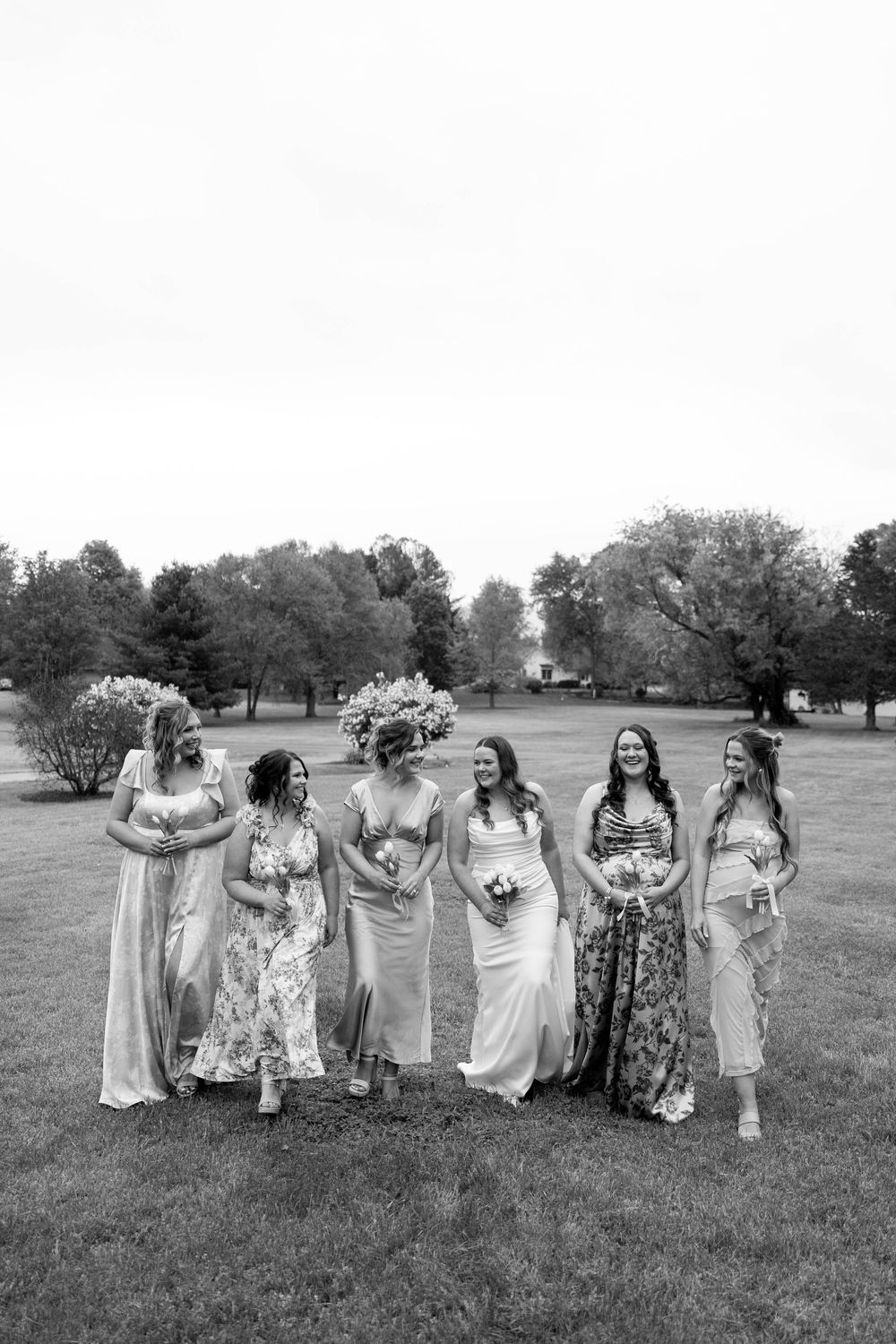 Bride and five bridesmaids laughing together on green lawn in black and white wedding photo.