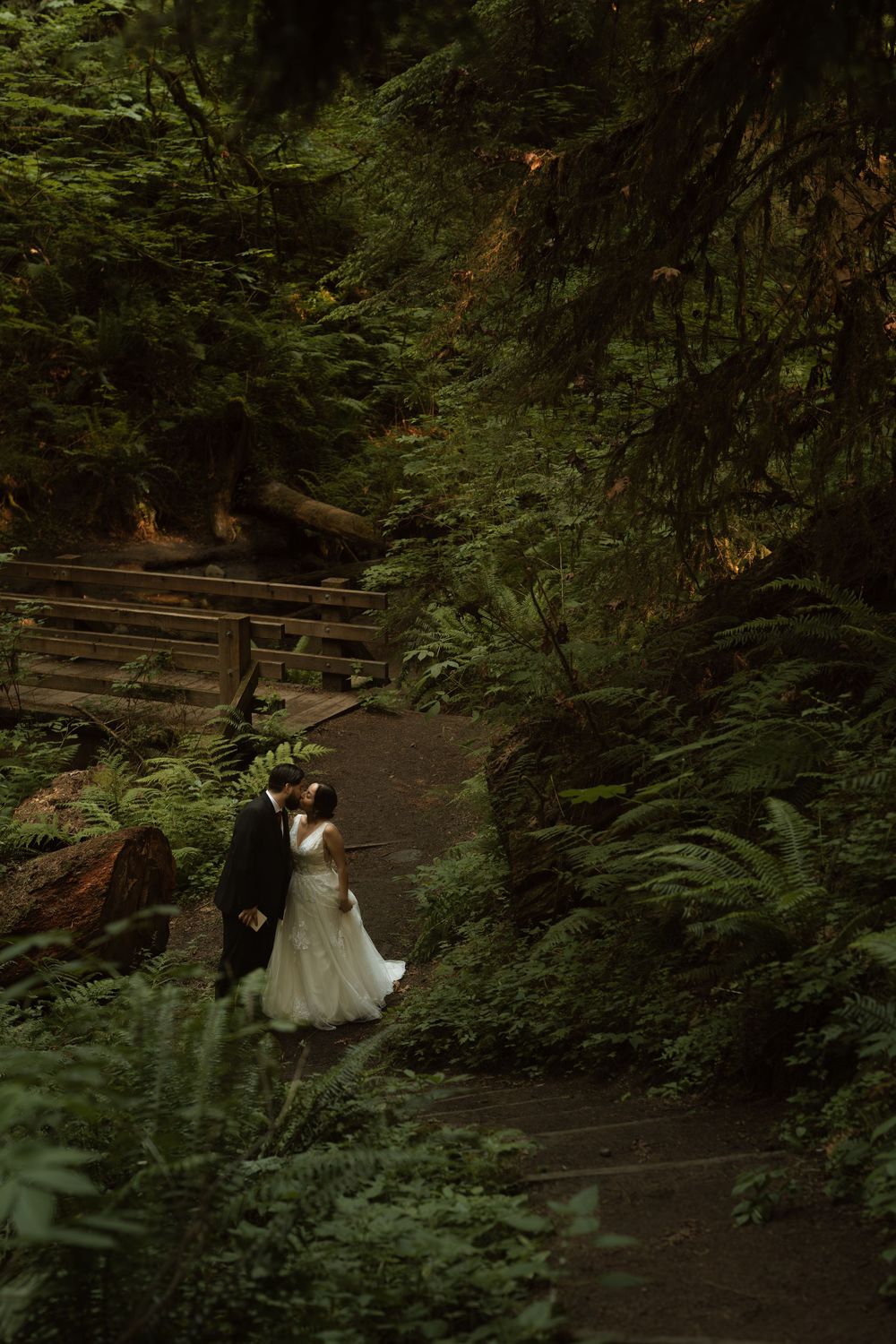 Bride and groom walk hand in hand through a lush green forest on their wedding day.