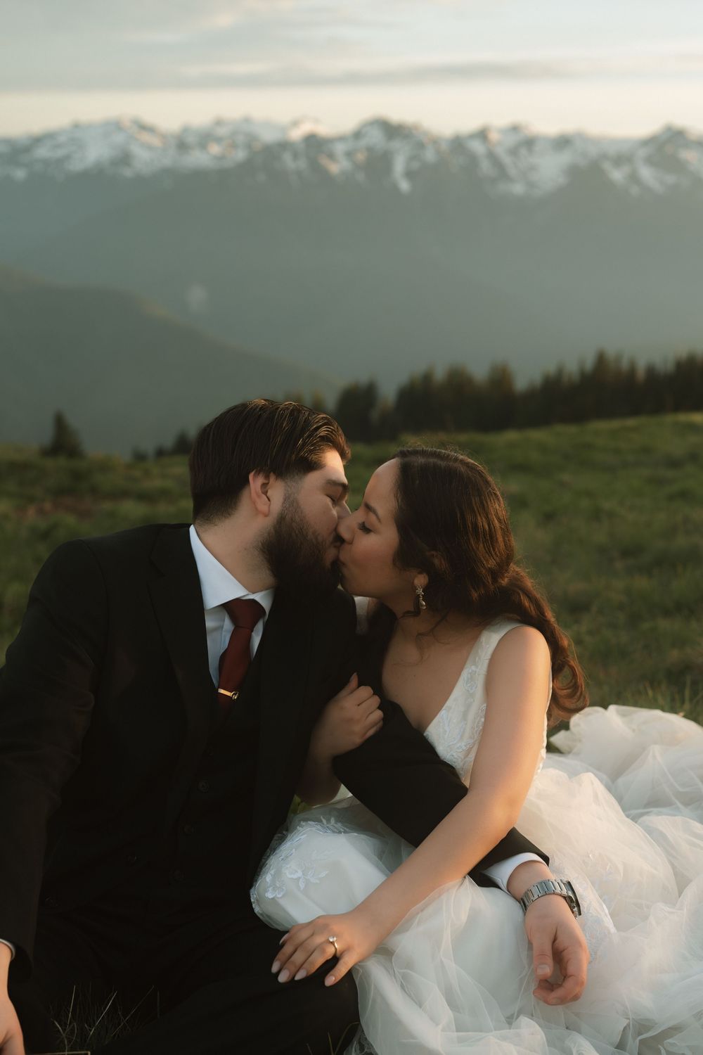 Bride and groom share a romantic kiss on a mountain meadow with snow-capped peaks in the background.