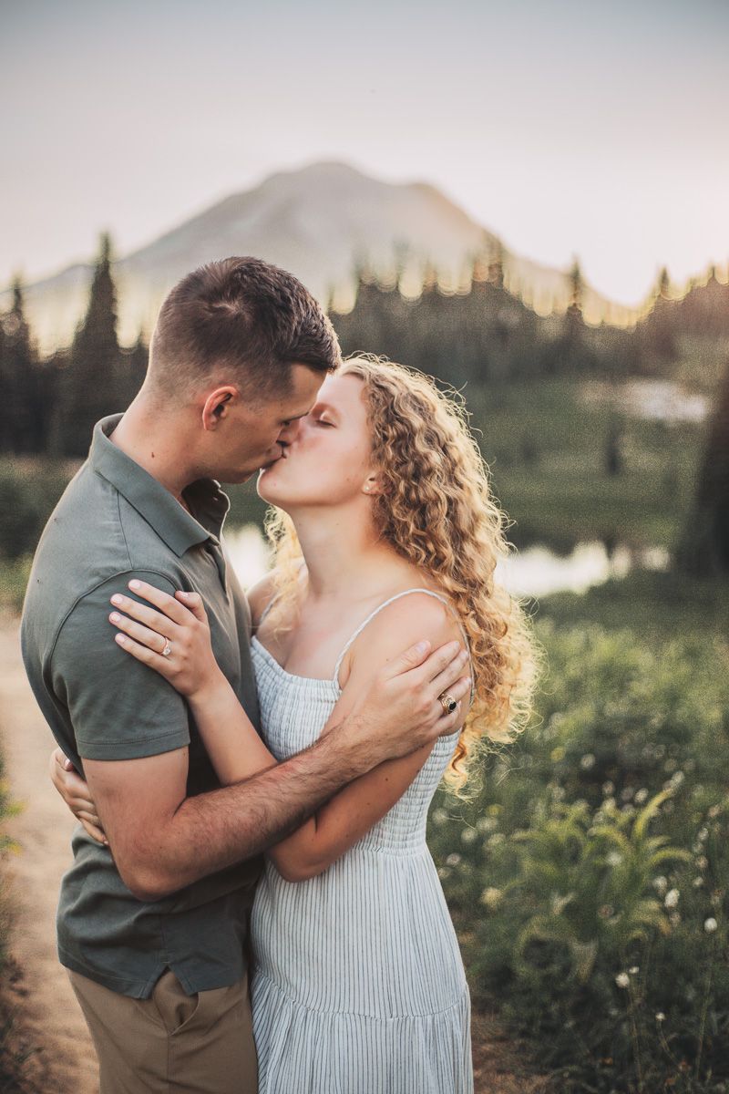 Couple sharing a kiss near a alpine lake at sunset with Mount Rainier visible in the background.