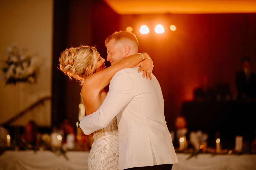 Bride and groom share their first dance, embracing tenderly under warm amber wedding reception lighting.