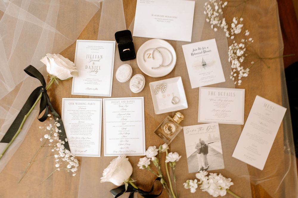 Elegant wedding stationery flatlay with invitations, rings, and white roses on a marble surface.