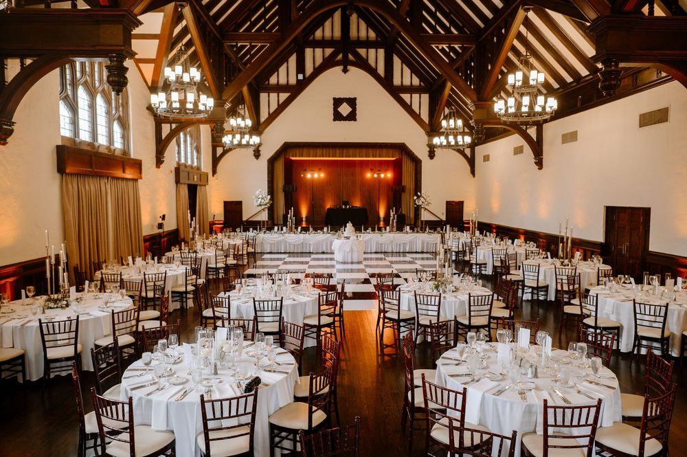 Elegant wedding reception hall with round tables, white linens, chiavari chairs, and chandelier lighting in a historic venue.