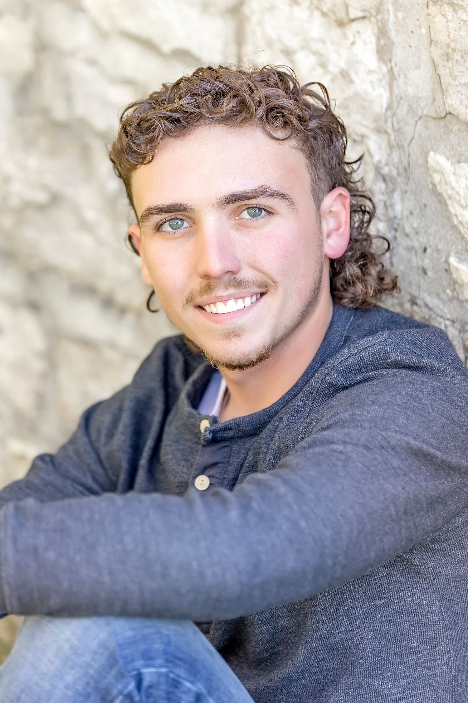 High school senior boy posing against a stone wall during a senior portrait session in North Iowa.