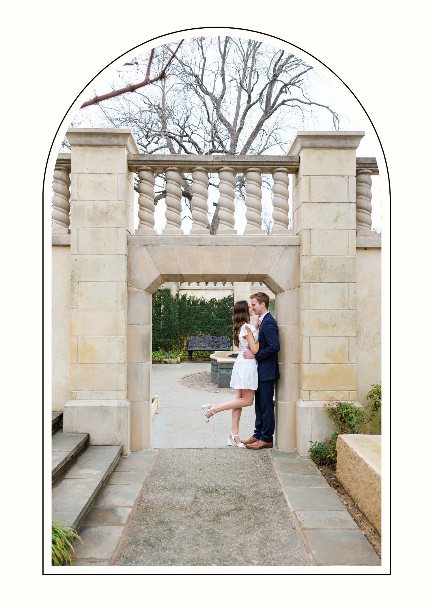 Engaged couple embracing under a structural arch in a botanic garden