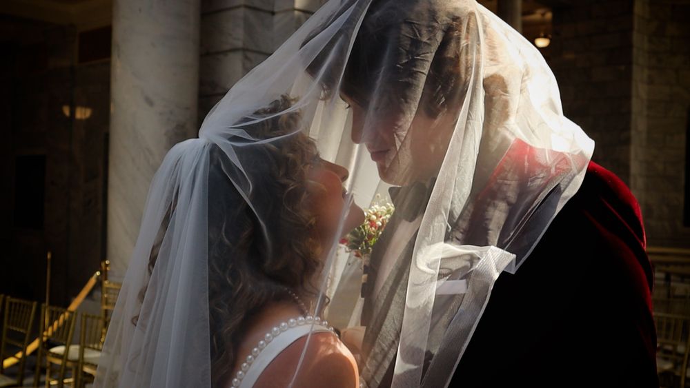 Bride and groom sharing a romantic kiss under a flowing white wedding veil at an elegant venue.