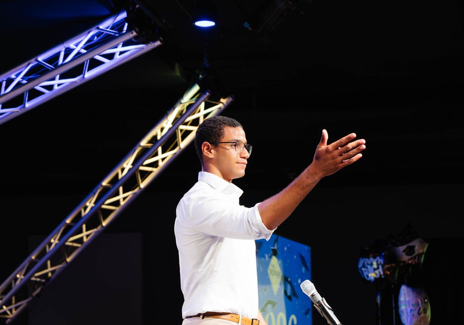 Young man in white shirt speaking at a podium during a professional conference or event on stage.