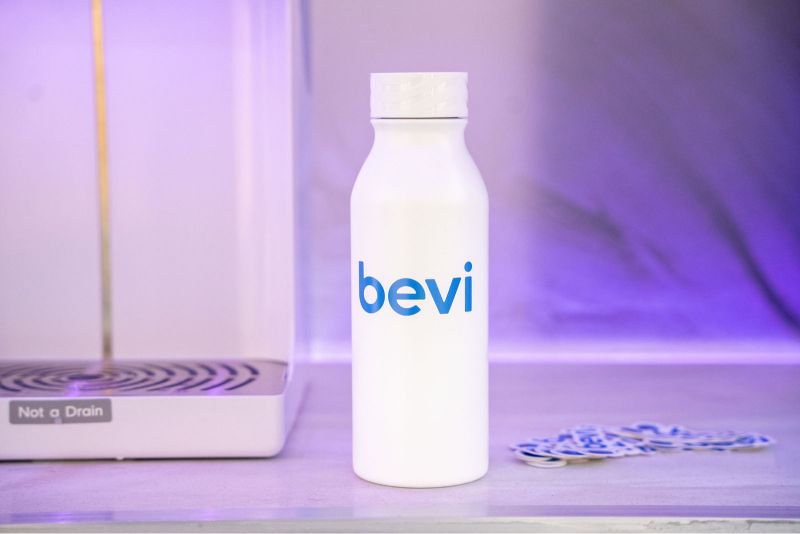 White Bevi branded reusable water bottle on a shelf with purple ambient lighting.