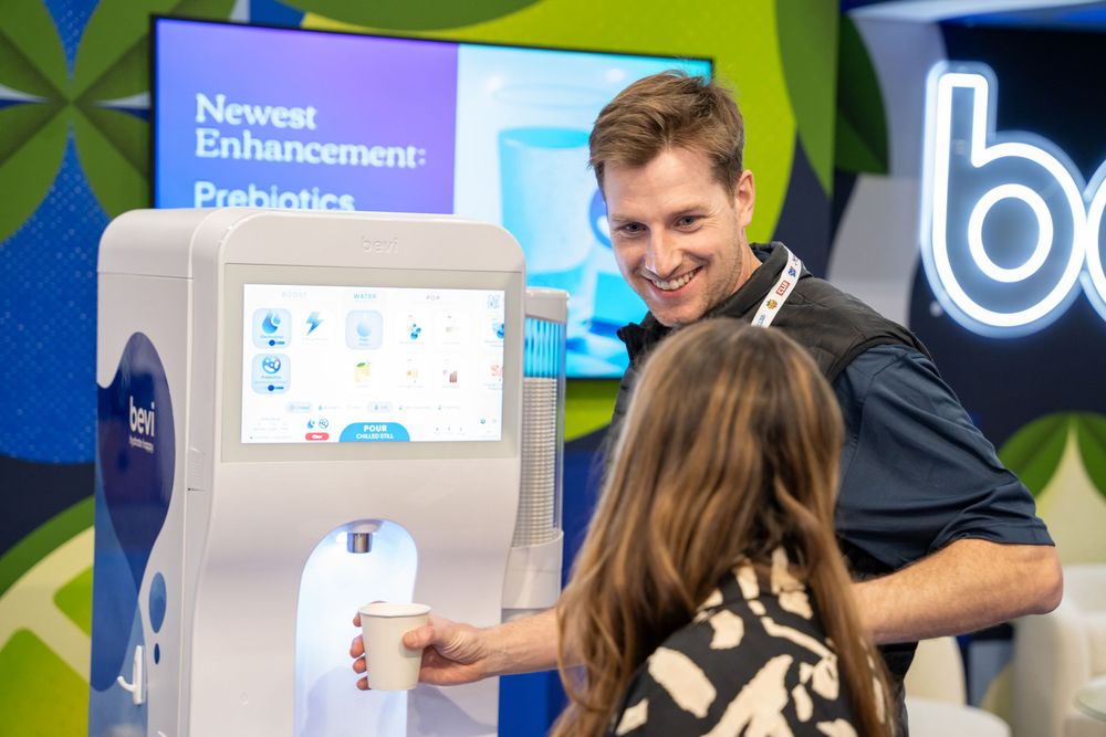 Man demonstrates a smart beverage dispenser with prebiotics enhancement at a trade show exhibit.