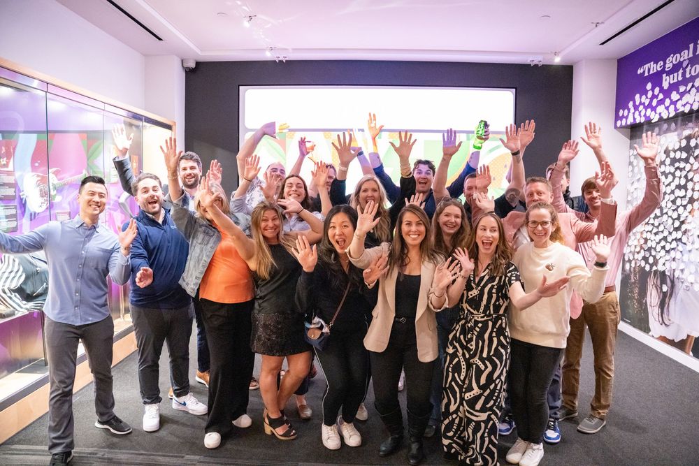 A large group of cheerful people celebrating together in a modern event space with colorful wall art.