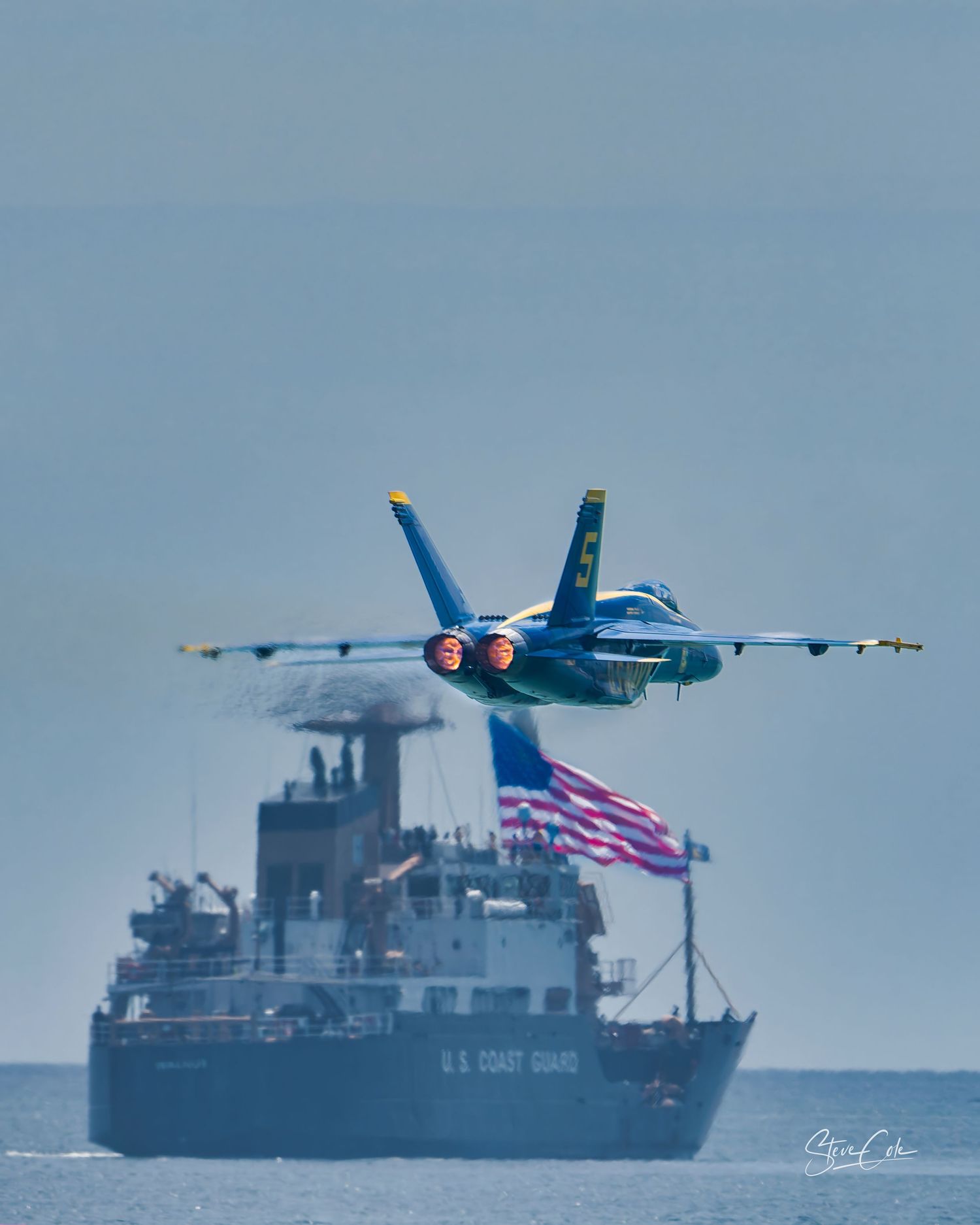 Blue Angels F/A-18 jet with afterburners glowing flying low over a US Coast Guard ship, fine art photography by Steve Cole Photography.