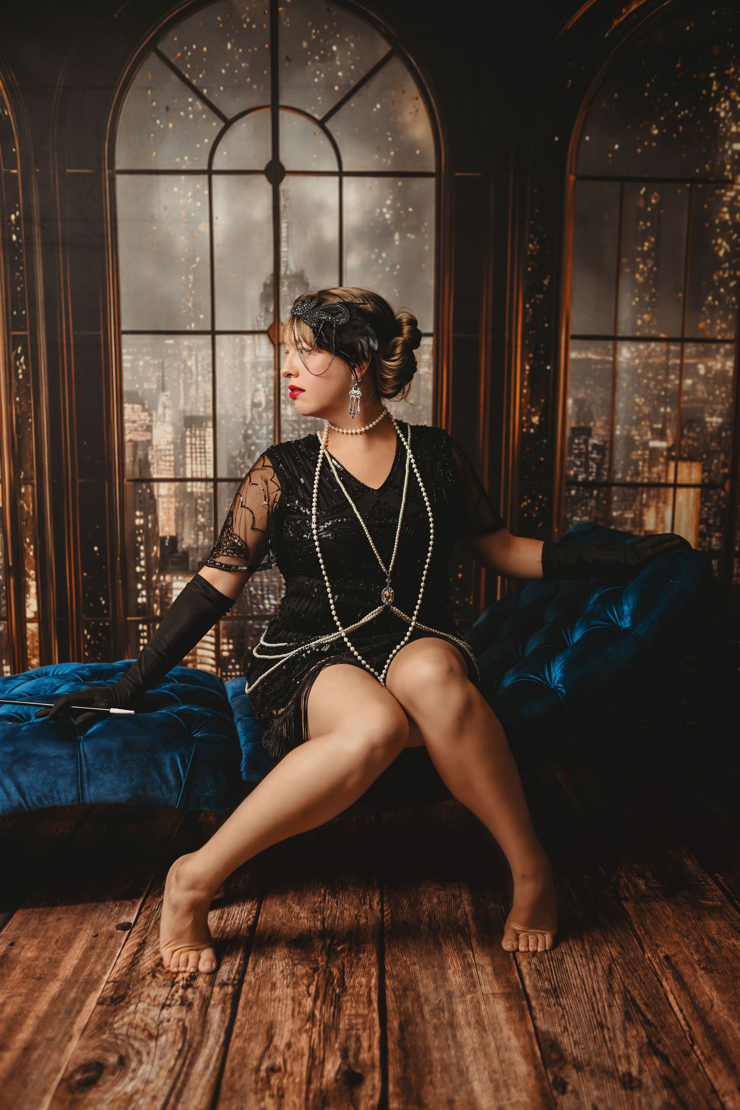 Redhead woman in plaid skirt, black blazer, and red heels sitting on vintage desk against brick wall.