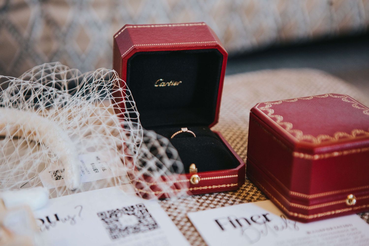 Cartier engagement ring in a red luxury box with a wedding veil and documents on an elegant surface.