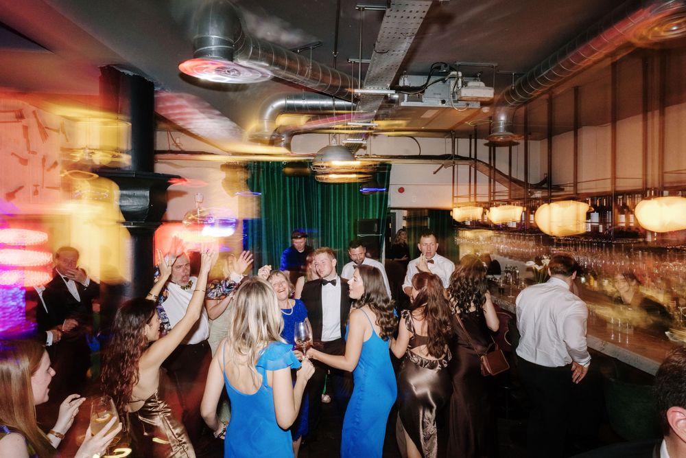 Guests dancing and socialising at an elegant indoor wedding reception with colourfu lighting at Pasture Restraint Bristol, St Mary Redcliffe