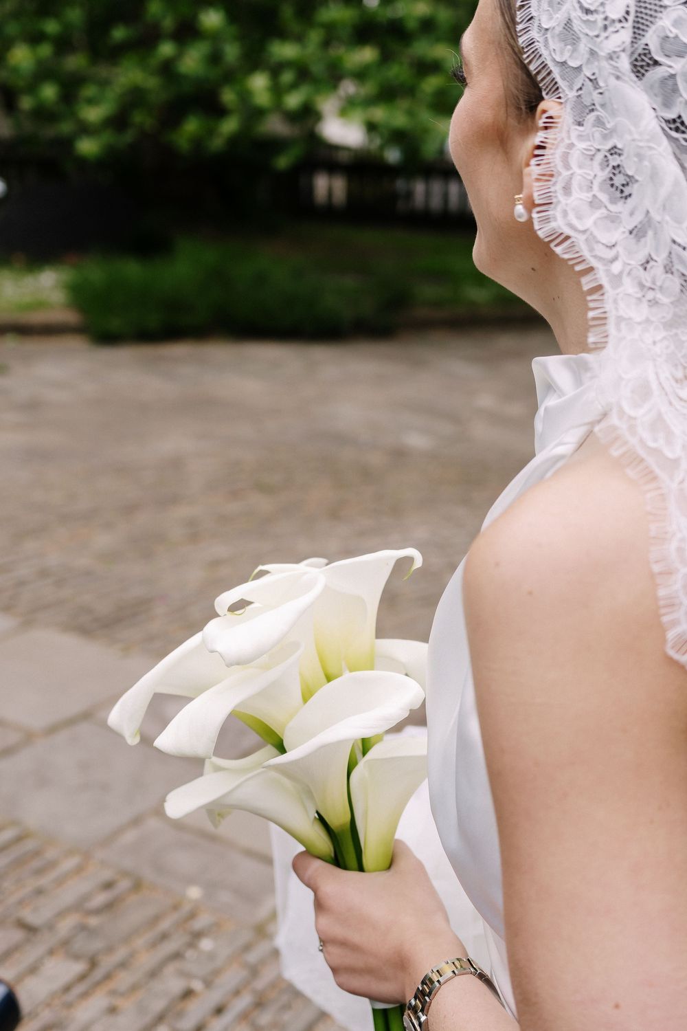 Bride in white lace veil holding elegant white calla lily bouquet outdoors on cobblestone path at St Mary Redcliffe Church Bristol Wedding