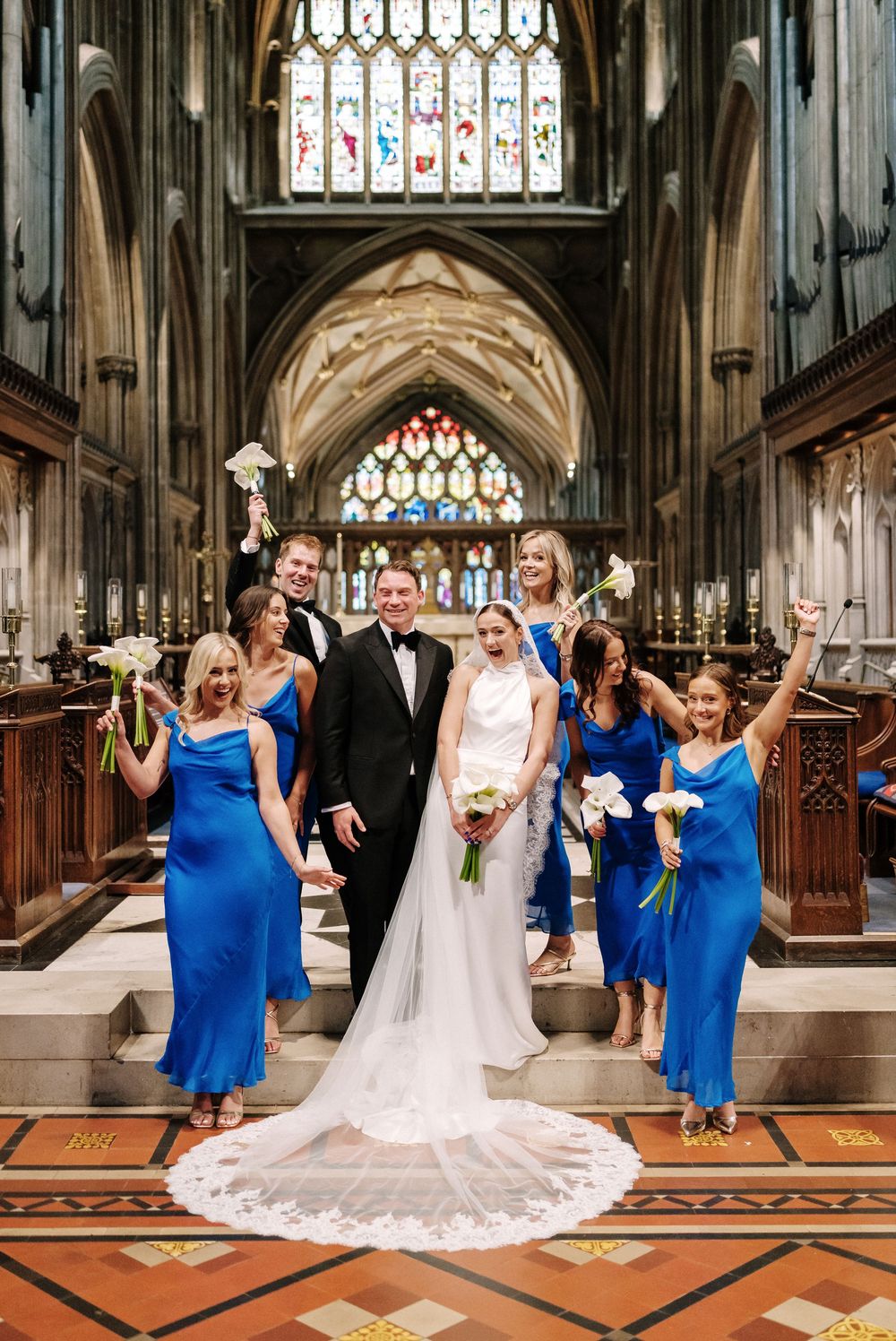 Bride and groom pose with bridesmaids in blue dresses and groomsmen inside St Mary Redcliffe Church, Bristol Wedding