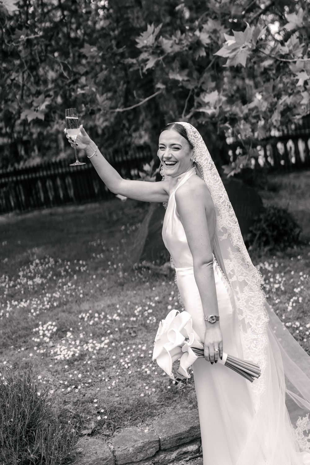 Black and white photo of a smiling bride in a veil raising a champagne glass at St Mary Redcliffe Church Bristol Wedding