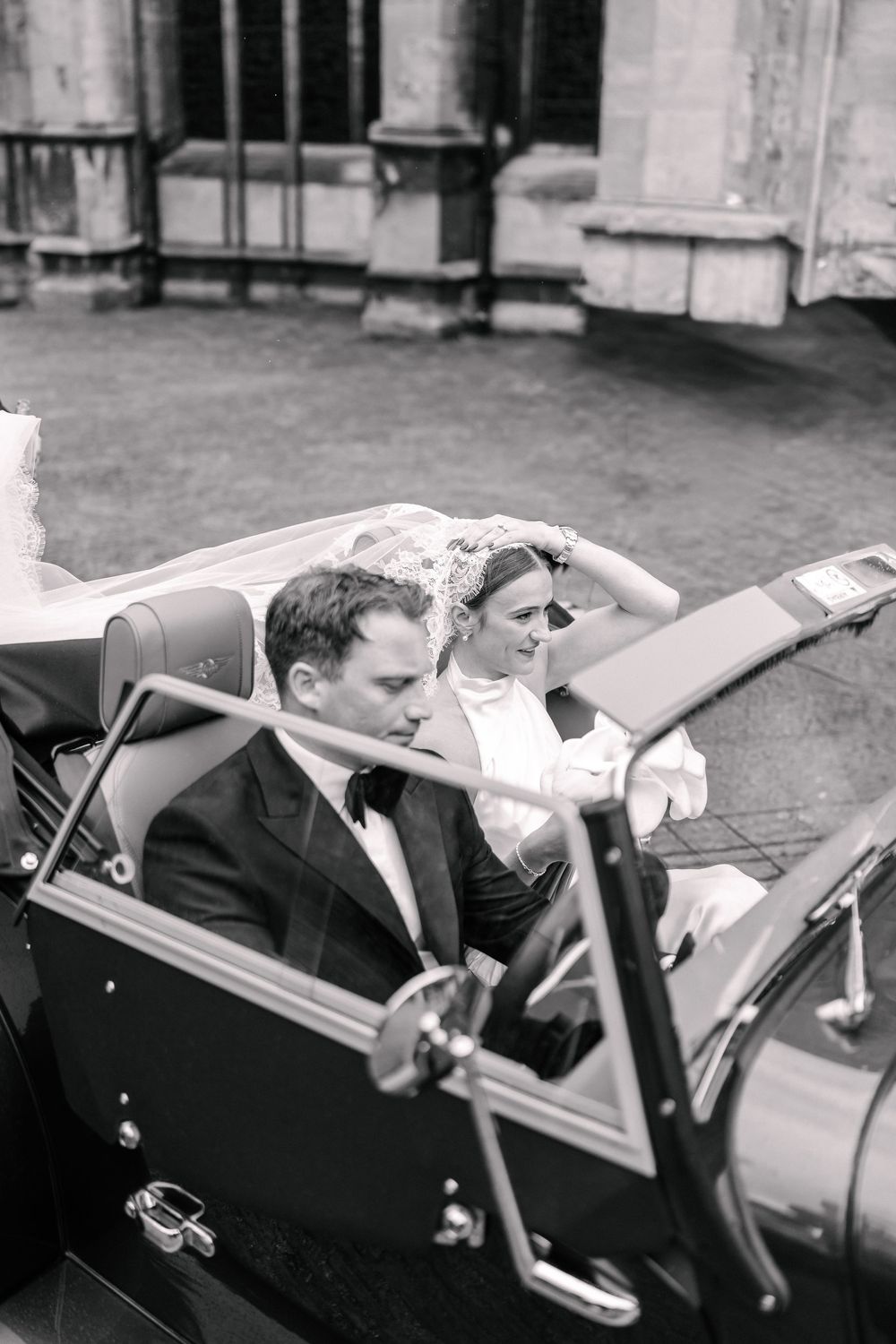 Black and white photo of a bride and groom riding in a vintage convertible at their St Mary Redcliffe Church, Bristol Wedding
