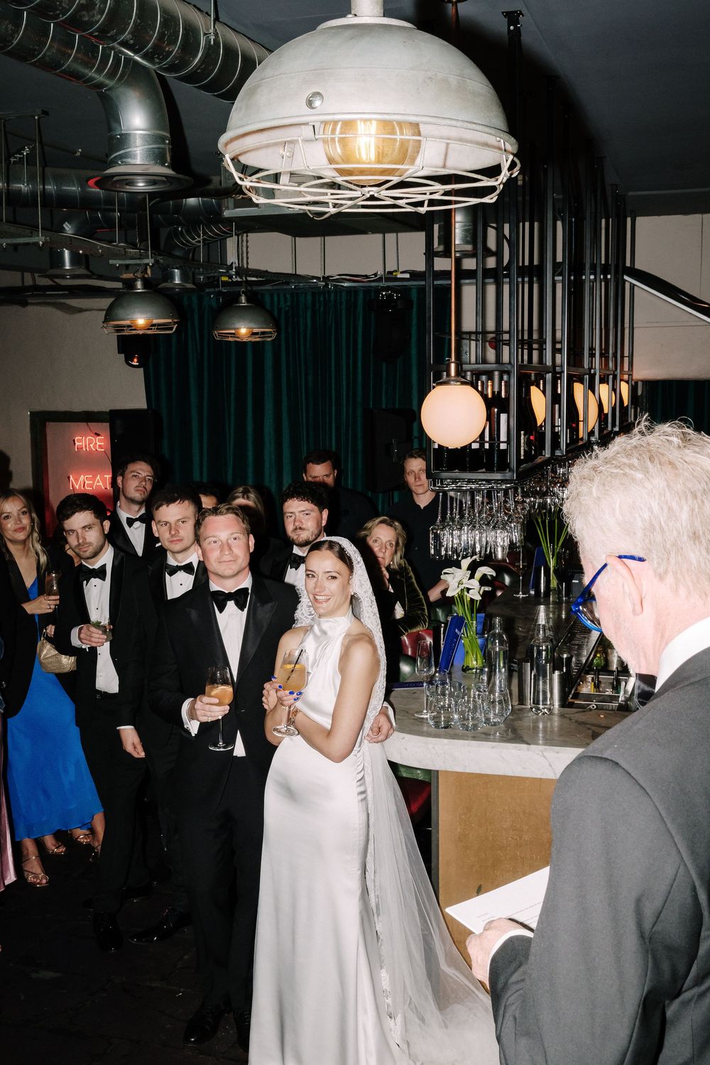 Bride and groom stand before officiant during indoor wedding reception at Pasture Bristol, guests in formal attire gathered behind them.