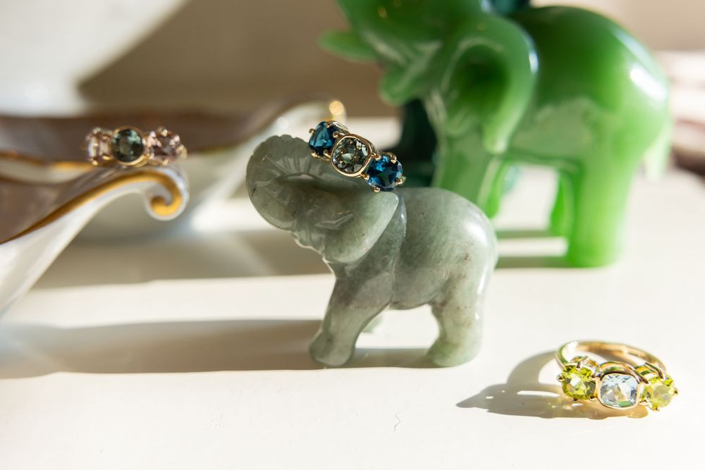 Small jade elephant figurine wearing blue gemstone gold rings on a white surface.