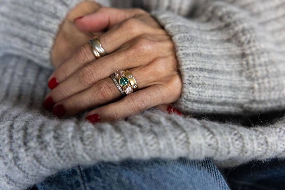 Close-up of hands wearing gold gemstone and silver rings over a gray knit sweater.