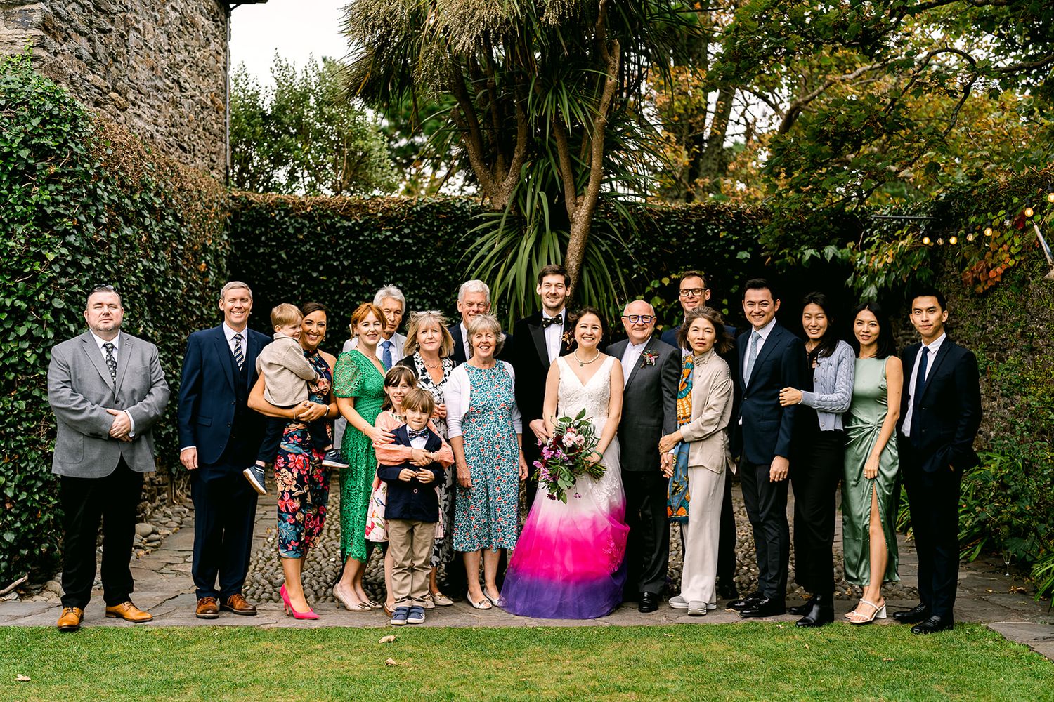 A group stands together on a lawn for a formal outdoor event with greenery behind them.