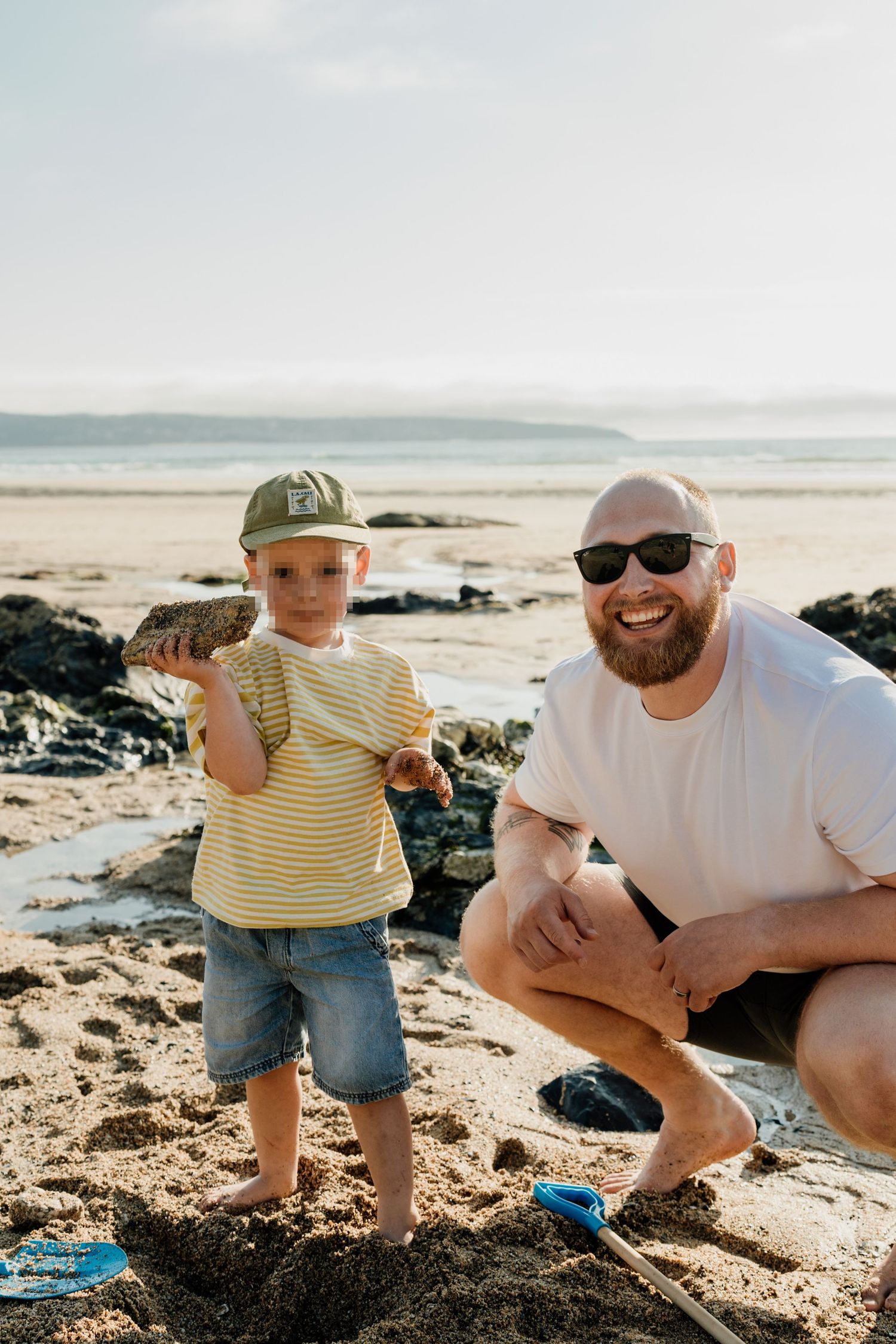 A bearded father and young son smiling at the camera on Gwithian Beach, during family photoshoot in cornwall.