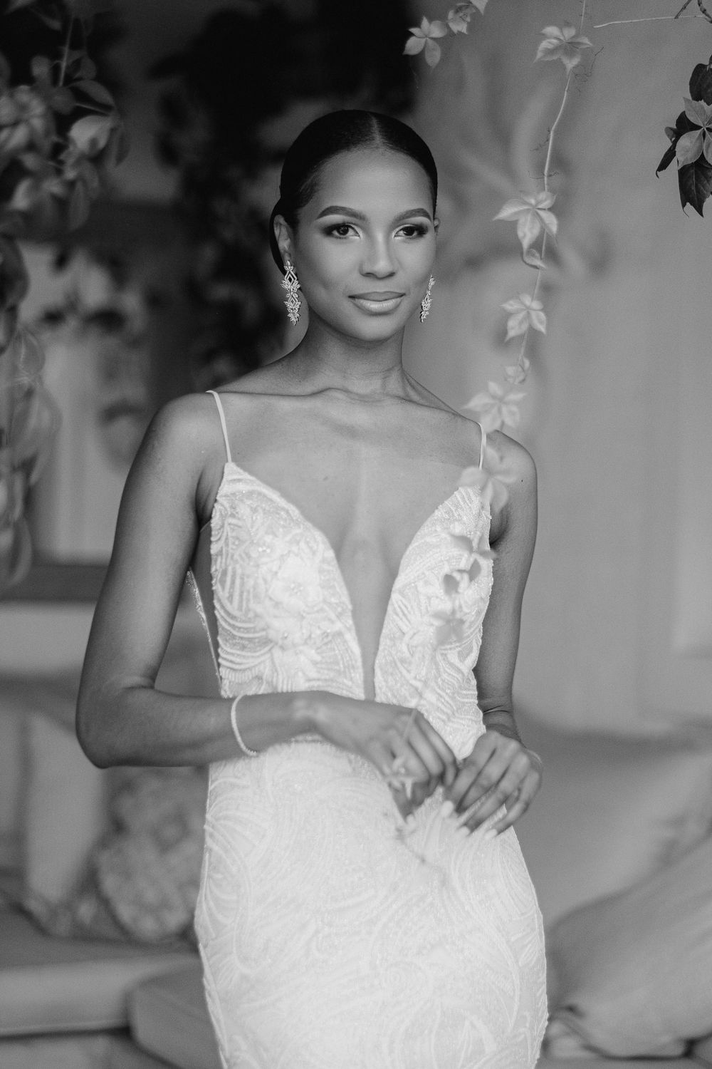 Elegant bride in a beaded deep-V wedding gown with spaghetti straps, black and white portrait.