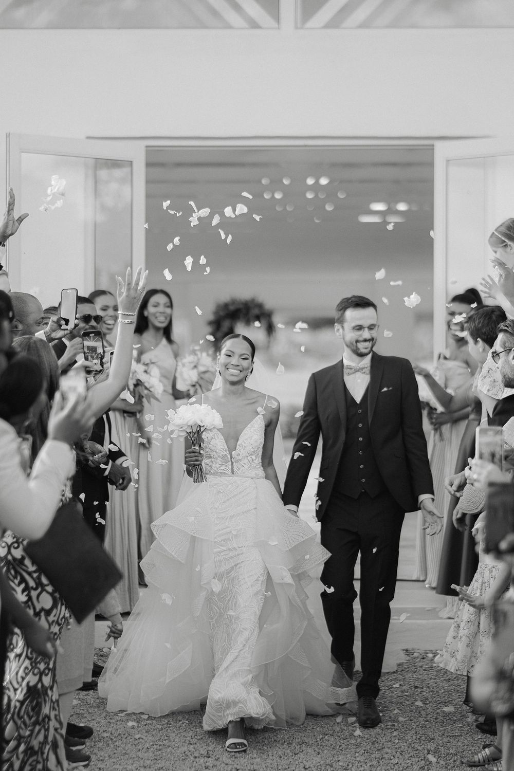 Newlyweds exit ceremony as guests toss confetti in joyful black and white wedding photo.