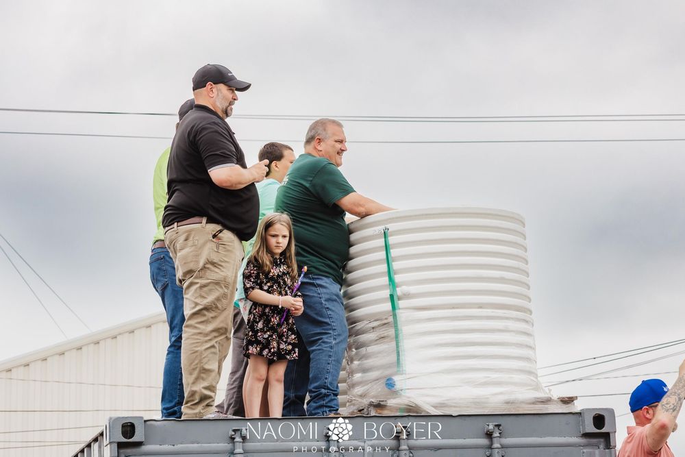 Group of adults and a young girl standing on a flatbed trailer outdoors near a large white silo.