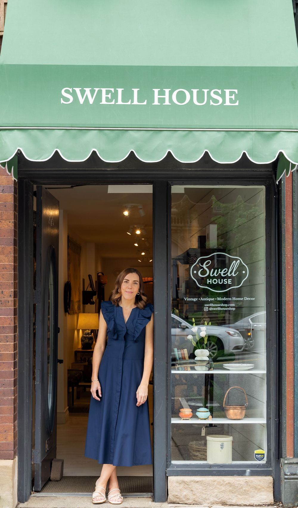 Woman in navy dress standing in doorway of Swell House La Grange vintage and antique home decor shop with green awning.