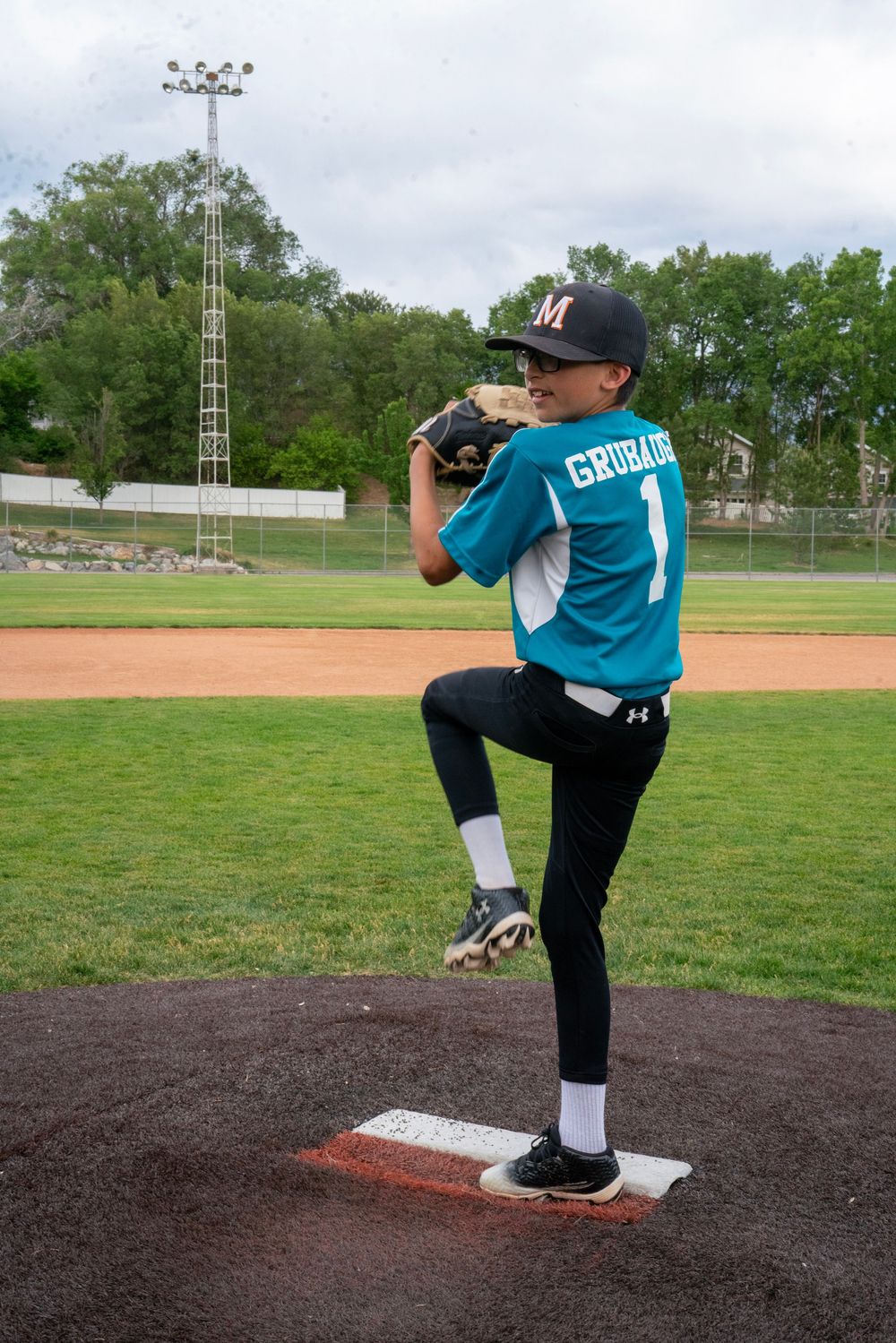 Young baseball pitcher in teal Grubacich number 1 jersey winds up on the mound.