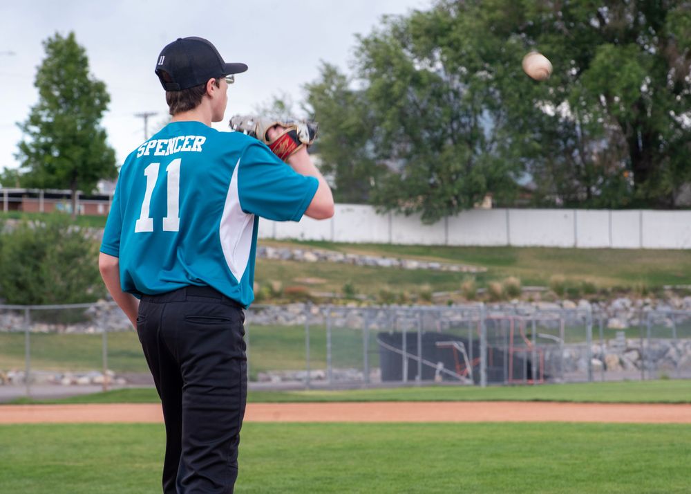 Baseball player wearing teal jersey number 11 throws ball on outdoor baseball field.