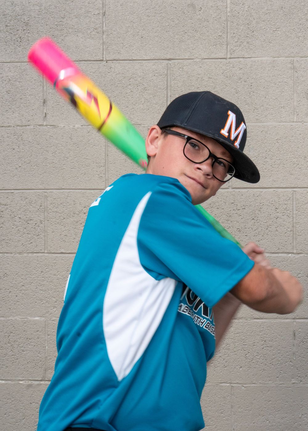 Young baseball player in teal Miami Marlins jersey poses with colorful bat over shoulder against concrete wall.
