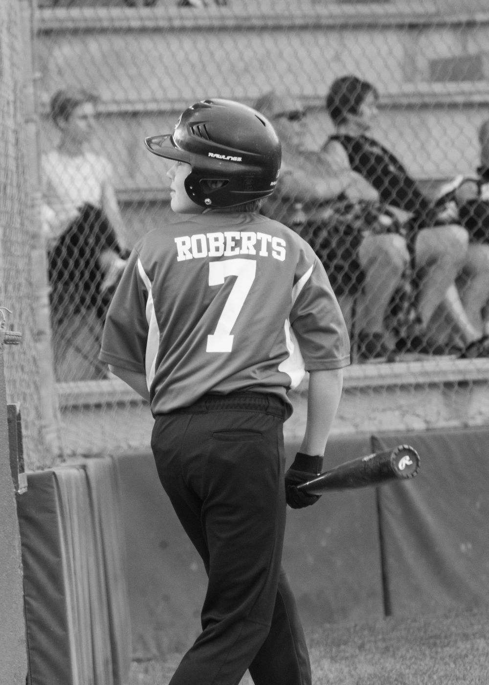 Black and white photo of youth baseball player Roberts number 7 holding bat in batting stance near dugout.