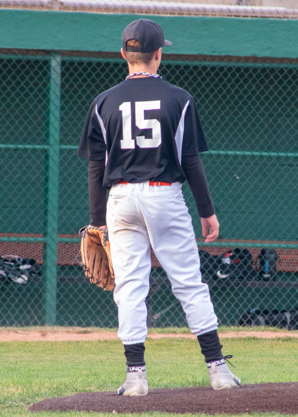 Baseball player wearing number 15 black jersey standing on field holding a glove.