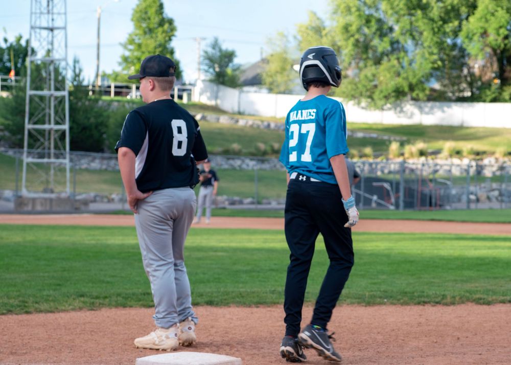 Two youth baseball players standing at base during a game in evening light.