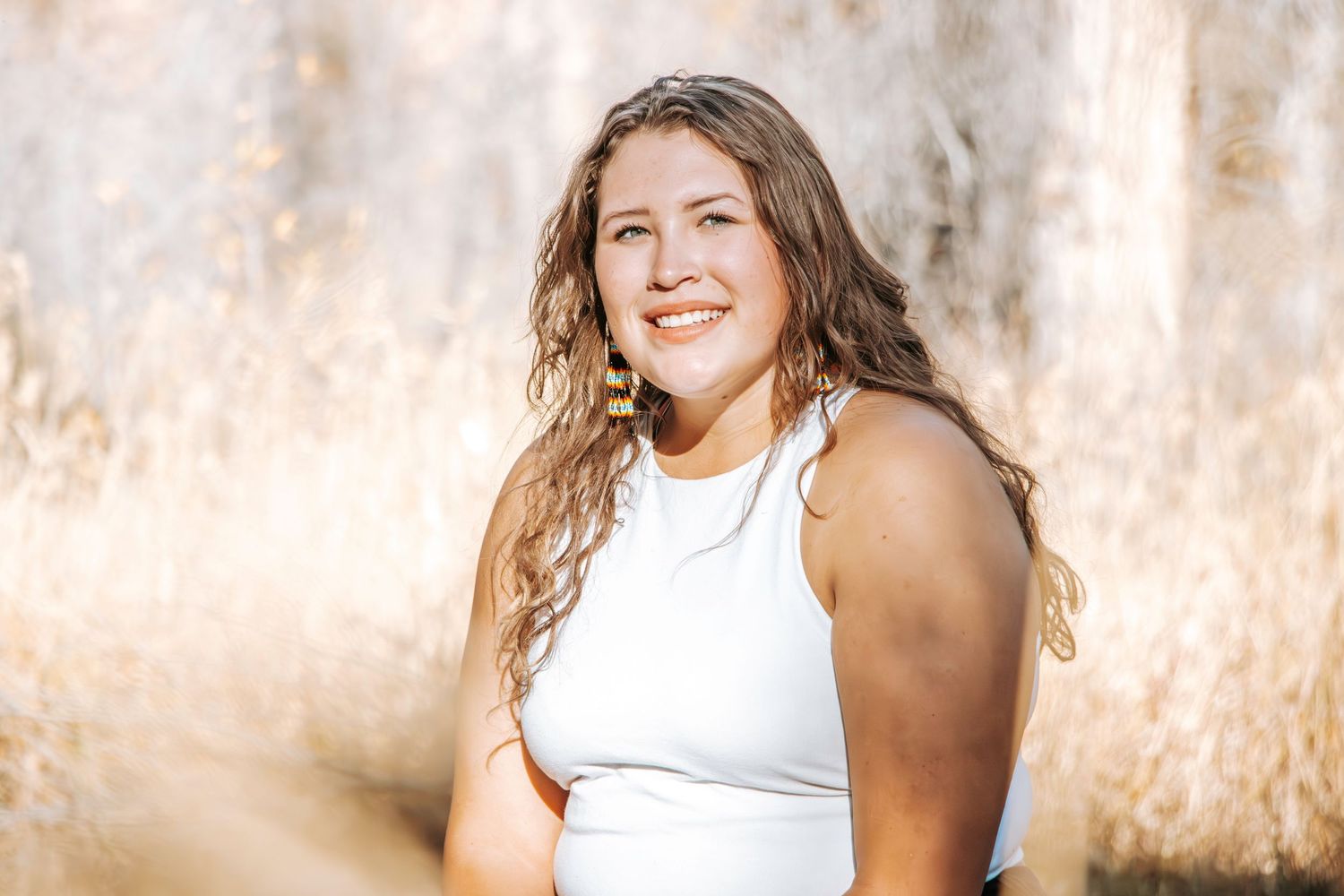 Portrait of person in white tank top smiling in golden natural lighting.